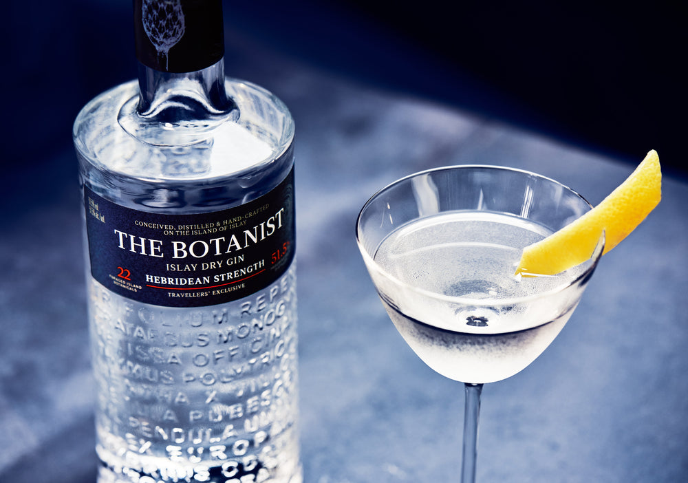 A bottle of Botanist Hebridean Strenght close to a cocktail glass, blue background