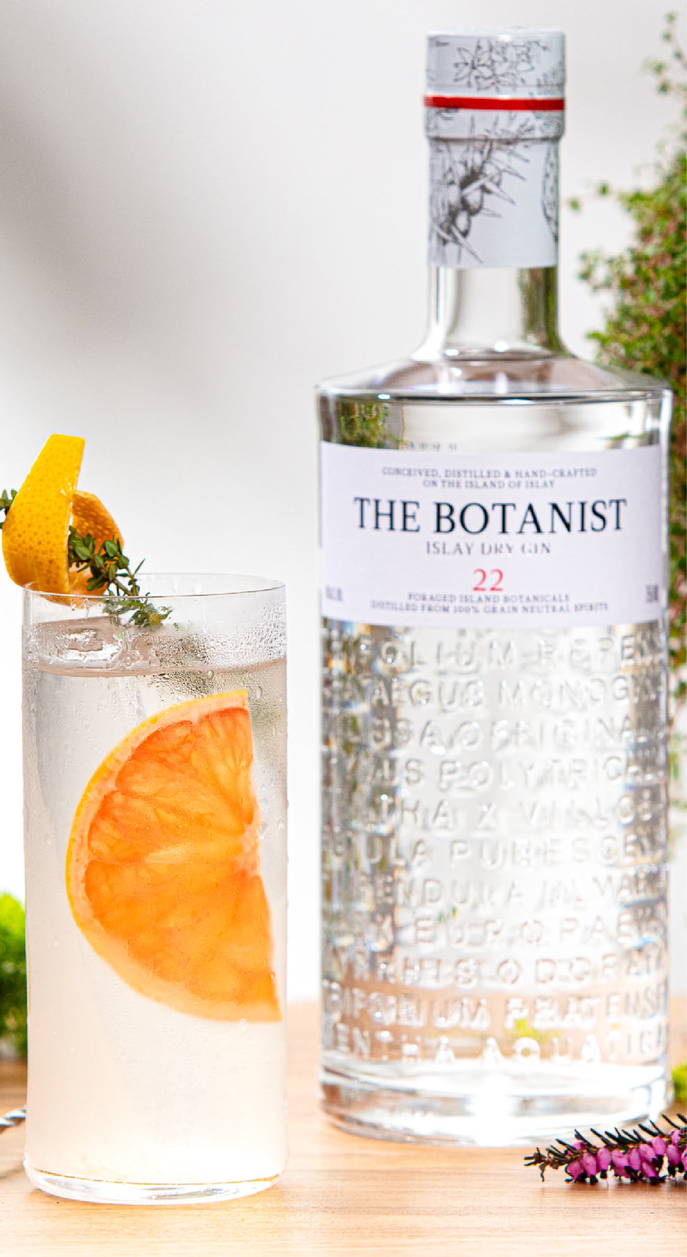 A lifestyle photo of a Botanist bottle close to a glass of cocktail with an orange slice